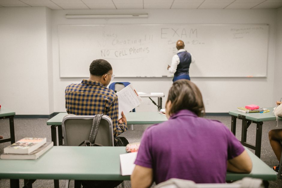 Students in a college classroom taking an exam with rules written on the board.